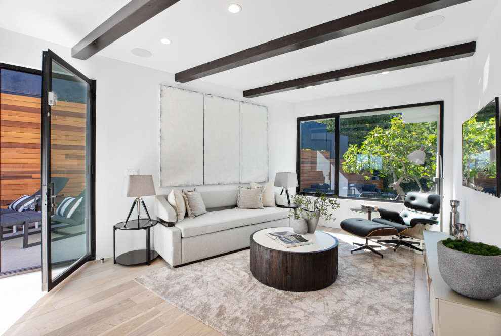 This is an example of a contemporary open plan living room in Los Angeles with white walls, light hardwood flooring, a wall mounted tv, beige floors and exposed beams.