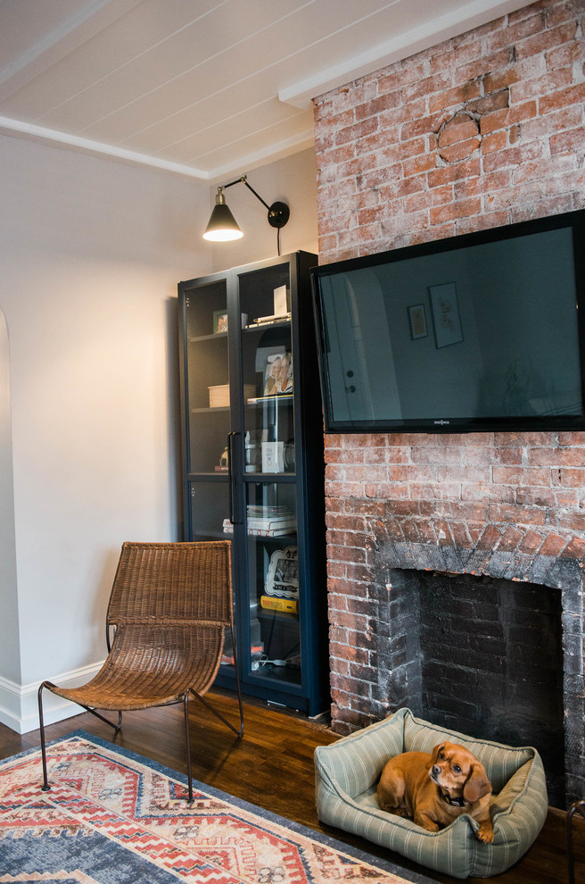 Cette photo montre un petit salon éclectique avec un mur gris, parquet foncé, une cheminée standard, un manteau de cheminée en brique et un téléviseur fixé au mur.