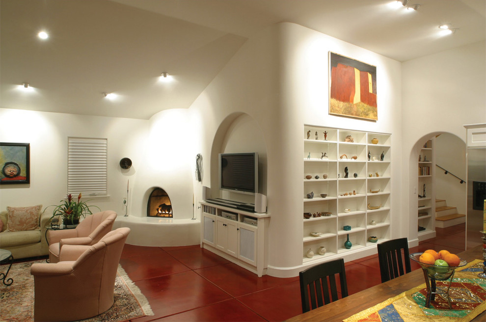 Cette image montre un salon sud-ouest américain avec sol en béton ciré, une cheminée d'angle, un mur blanc et un sol rouge.