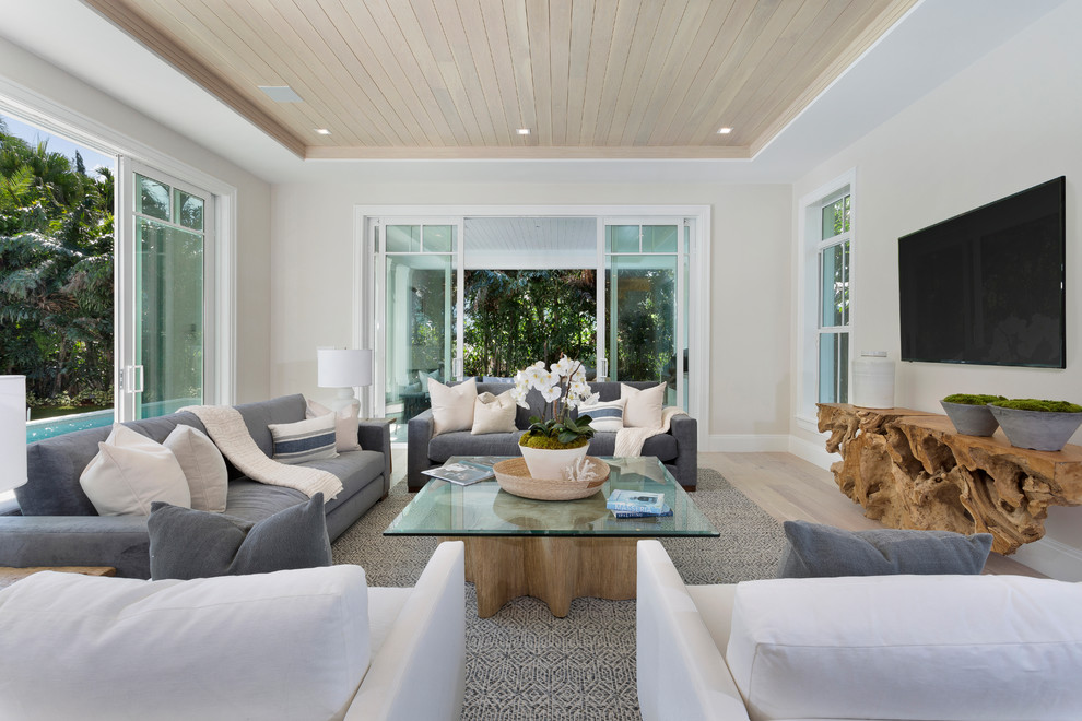 Beach style living room in Miami with white walls, light hardwood flooring, a wall mounted tv and beige floors.