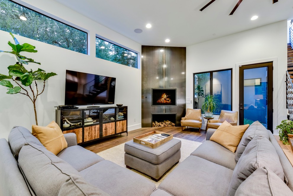 Idéer för vardagsrum, med vita väggar, mellanmörkt trägolv, en standard öppen spis, en spiselkrans i metall, en fristående TV och brunt golv