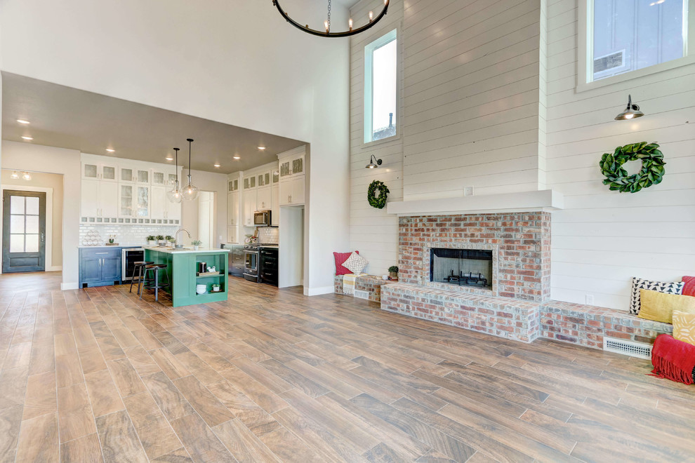 Idée de décoration pour un grand salon champêtre ouvert avec un mur multicolore, un sol en bois brun, une cheminée standard, un manteau de cheminée en brique et un sol marron.