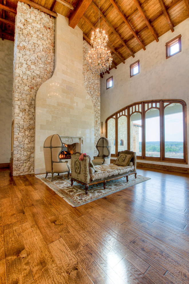 Diseño de salón para visitas tipo loft mediterráneo extra grande con suelo de madera clara, chimenea de doble cara y marco de chimenea de piedra