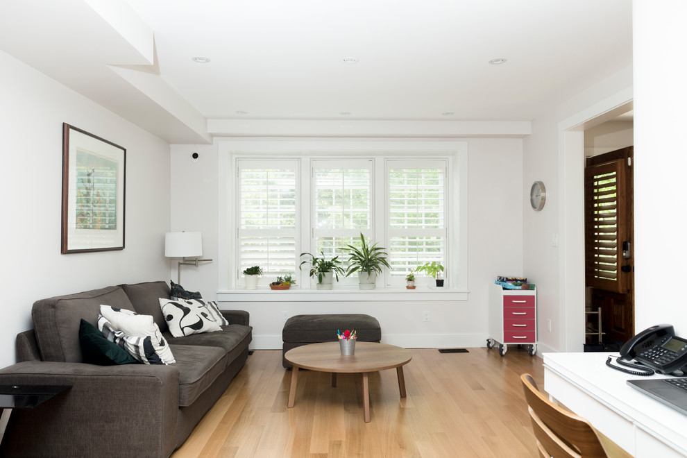 Modelo de salón abierto minimalista de tamaño medio con paredes blancas, suelo de madera clara y televisor colgado en la pared