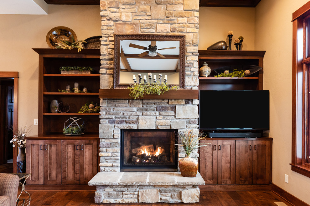 Example of a large arts and crafts open concept medium tone wood floor and brown floor living room design in Other with beige walls, a standard fireplace, a stone fireplace and a media wall