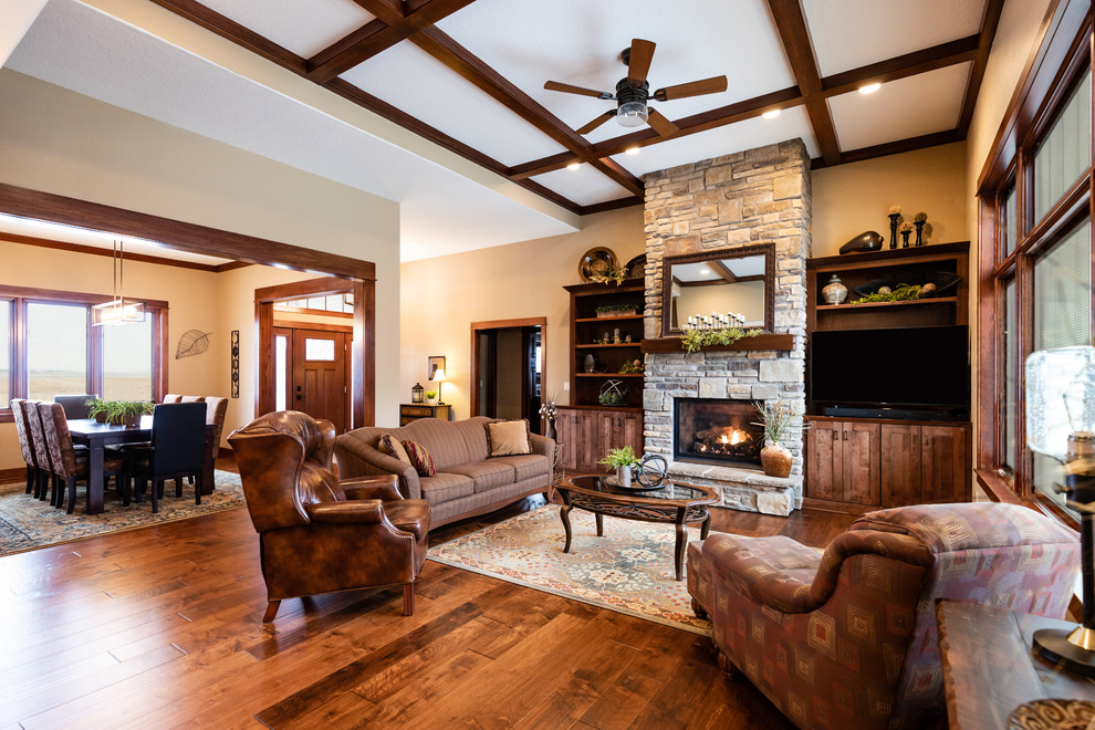 Aménagement d'un grand salon craftsman ouvert avec un mur beige, un sol en bois brun, une cheminée standard, un manteau de cheminée en pierre, un téléviseur encastré et un sol marron.