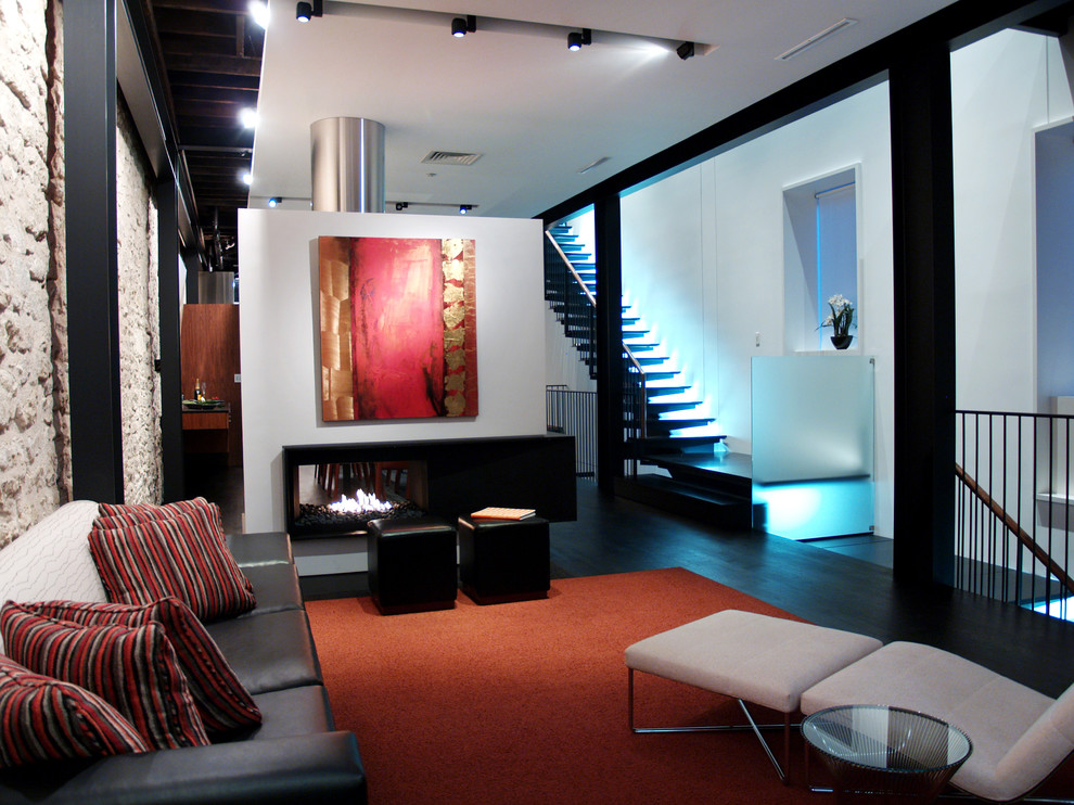 Cette image montre un salon design avec une salle de réception, un mur blanc, parquet foncé, une cheminée double-face, aucun téléviseur, un mur en pierre et un escalier.