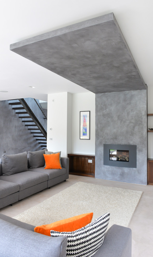 Ejemplo de salón abierto actual grande con paredes grises, suelo de cemento, todas las chimeneas, marco de chimenea de yeso y pared multimedia