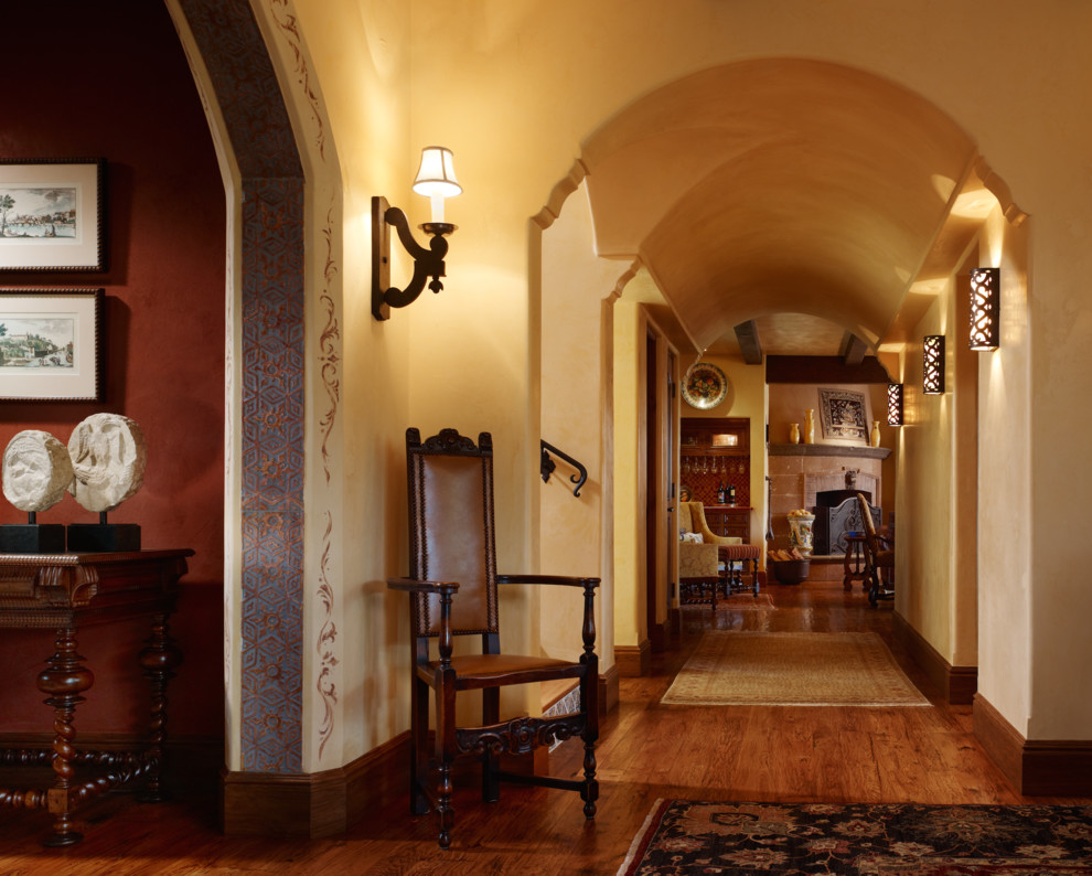 Exemple d'un grand salon méditerranéen ouvert avec une salle de réception, un mur jaune, un sol en bois brun, une cheminée standard, un manteau de cheminée en pierre et aucun téléviseur.