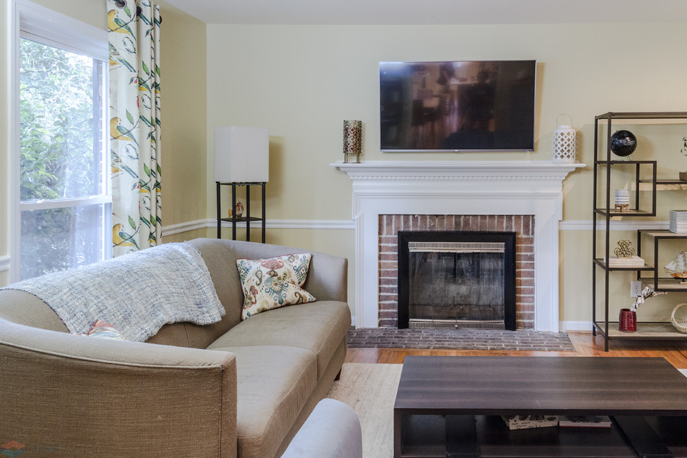 Photo of a medium sized traditional open plan living room in Charleston with yellow walls, light hardwood flooring, a standard fireplace, a brick fireplace surround, a wall mounted tv and brown floors.