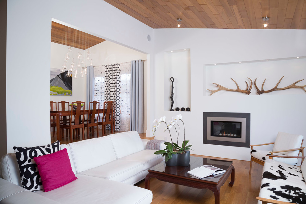 Modelo de salón actual de tamaño medio sin televisor con paredes blancas, suelo de madera clara, chimenea lineal y marco de chimenea de yeso