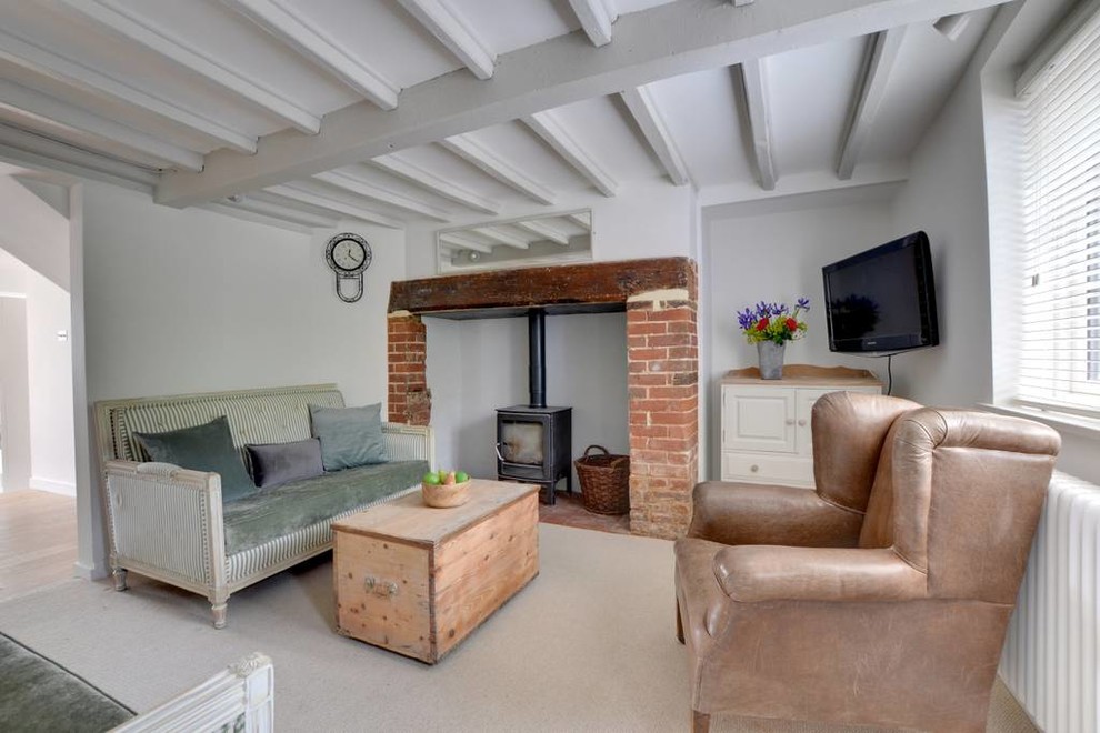 Kleines, Abgetrenntes Country Wohnzimmer mit weißer Wandfarbe, Teppichboden, Kaminofen, TV-Wand und beigem Boden in Kent