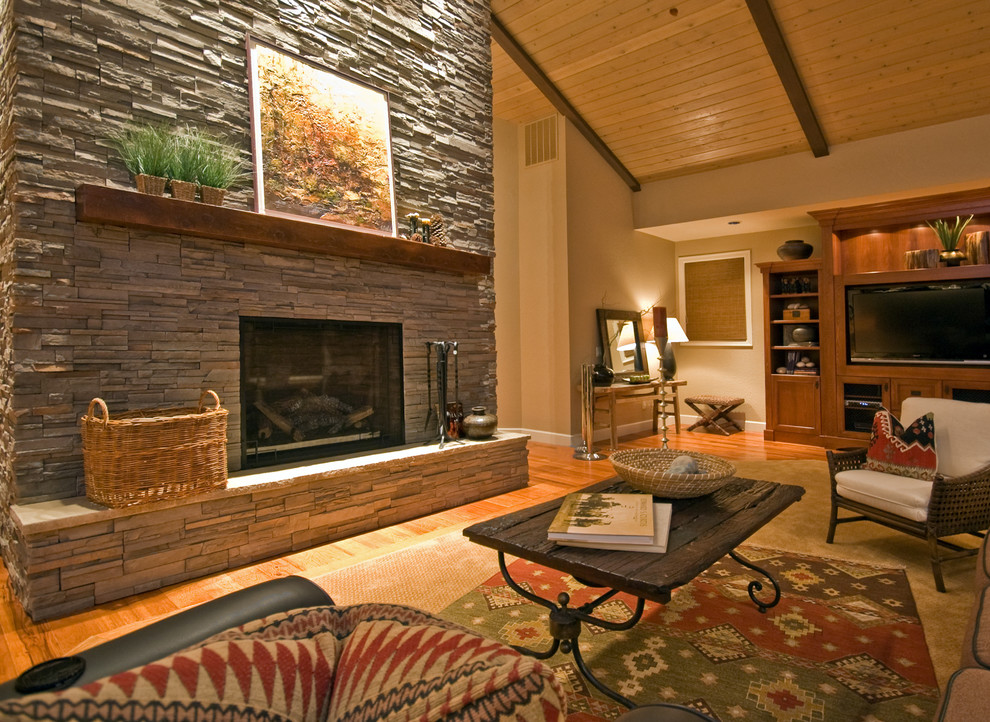 Ejemplo de salón abierto de estilo americano grande con paredes beige, suelo de madera en tonos medios, chimenea lineal, marco de chimenea de piedra y pared multimedia