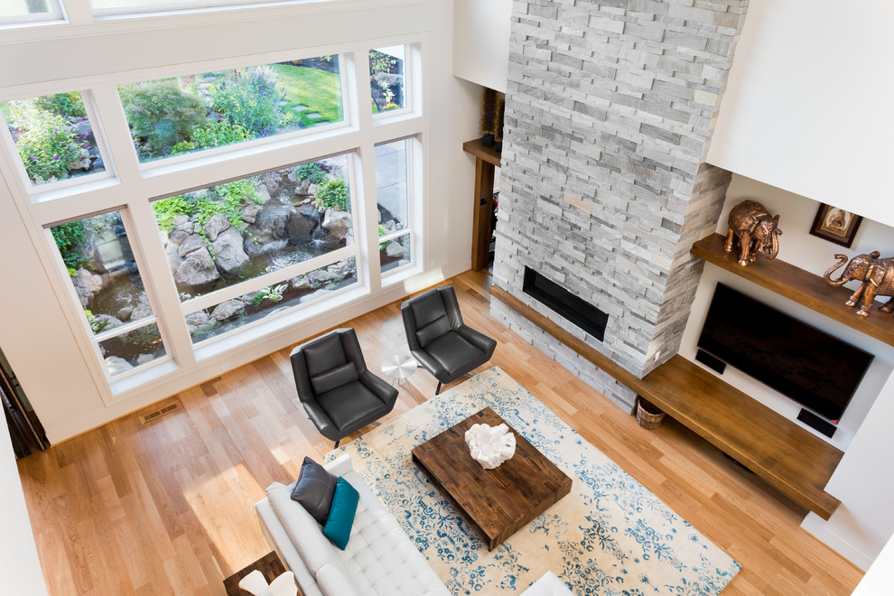 Стильный дизайн: огромная двухуровневая гостиная комната в современном стиле с белыми стенами, светлым паркетным полом, стандартным камином, фасадом камина из камня и телевизором на стене - последний тренд