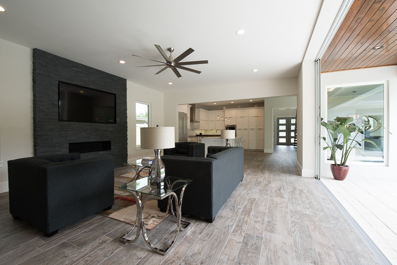 Offenes Modernes Wohnzimmer mit weißer Wandfarbe, Porzellan-Bodenfliesen, Kaminumrandung aus Stein und TV-Wand in Orlando