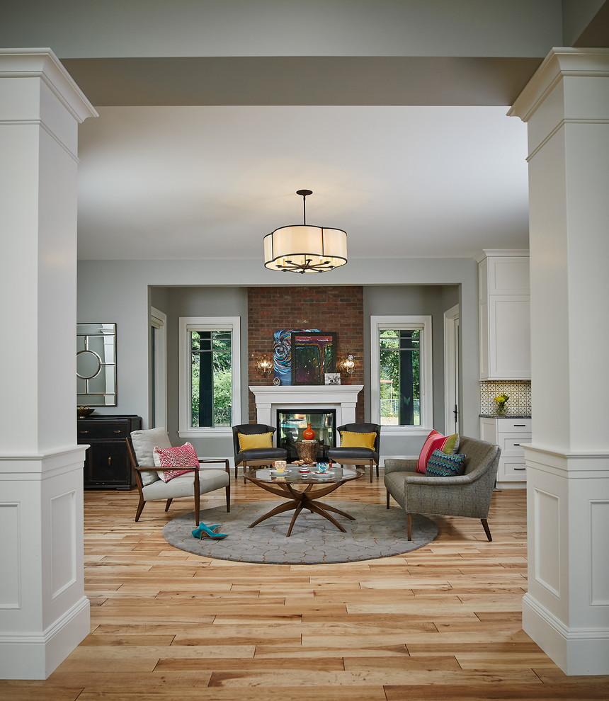 На фото: открытая гостиная комната в стиле неоклассика (современная классика) с серыми стенами, стандартным камином, фасадом камина из дерева и коричневым полом с