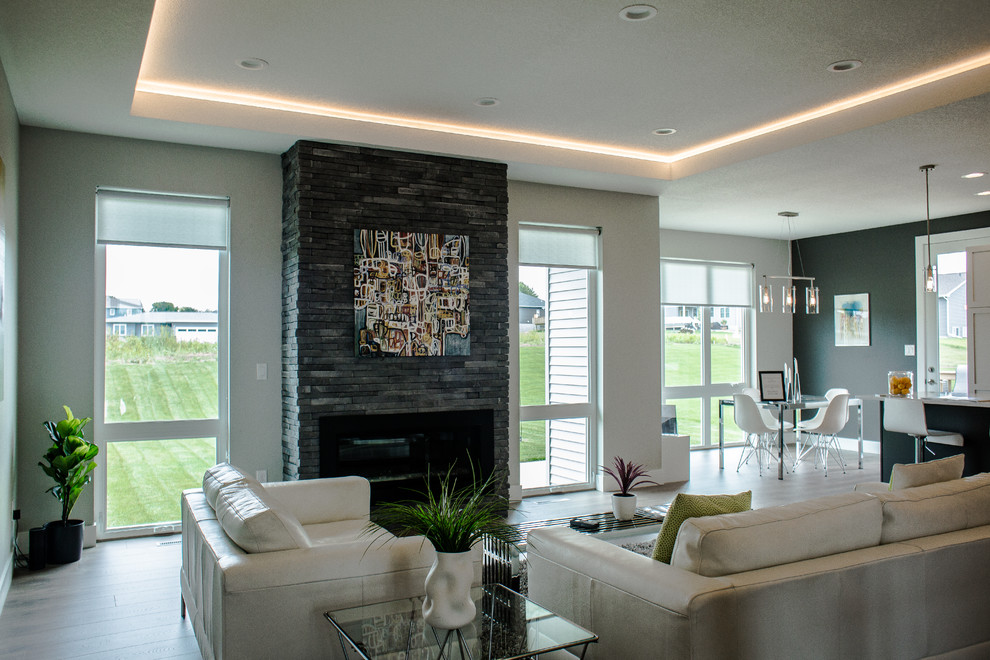 На фото: большая открытая гостиная комната в современном стиле с серыми стенами, паркетным полом среднего тона, стандартным камином, фасадом камина из камня и коричневым полом без телевизора