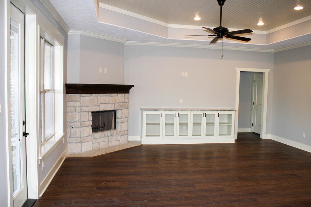 Cette photo montre un salon chic de taille moyenne et ouvert avec un mur gris, un sol en vinyl, une cheminée d'angle, un manteau de cheminée en pierre, un téléviseur fixé au mur et un sol marron.