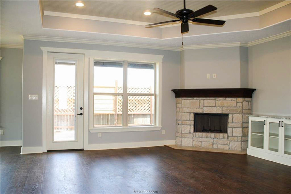 Пример оригинального дизайна: открытая гостиная комната среднего размера в классическом стиле с серыми стенами, полом из винила, угловым камином, фасадом камина из камня, телевизором на стене и коричневым полом