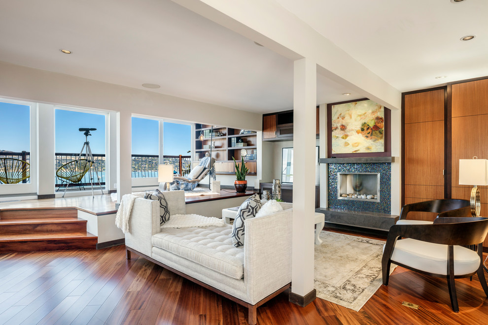 Photo of a beach style open plan living room in San Francisco with white walls, dark hardwood flooring, a standard fireplace, a tiled fireplace surround and brown floors.