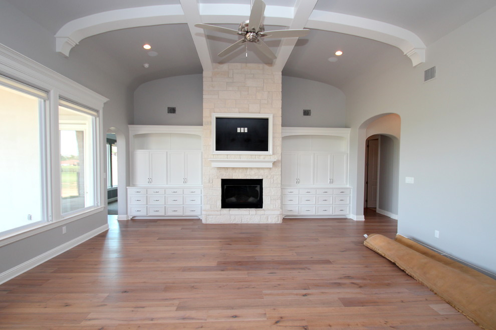 Example of a large open concept light wood floor living room library design in Dallas with gray walls, a standard fireplace, a stone fireplace and a wall-mounted tv