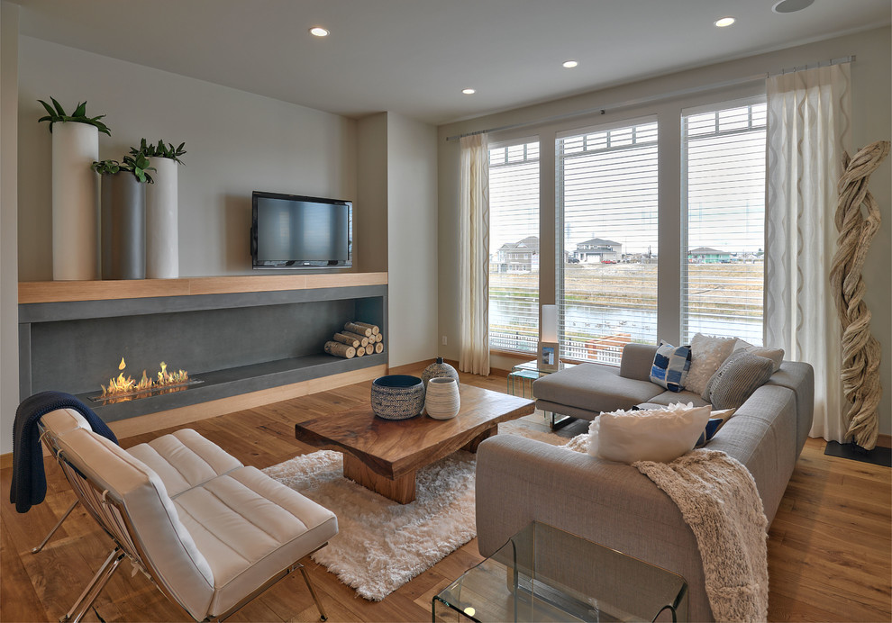Offenes Modernes Wohnzimmer mit beiger Wandfarbe, braunem Holzboden, Kaminumrandung aus Beton, freistehendem TV, braunem Boden und Gaskamin in Sonstige