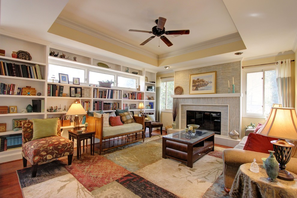 Exemple d'un grand salon chic ouvert avec une bibliothèque ou un coin lecture, un mur jaune, un sol en bois brun, une cheminée standard, un manteau de cheminée en carrelage et aucun téléviseur.