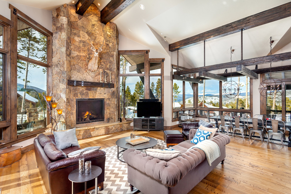 Cette photo montre un salon montagne ouvert avec un mur blanc, un sol en bois brun, une cheminée standard, un manteau de cheminée en pierre et un téléviseur indépendant.