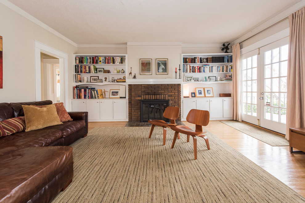 Diseño de biblioteca en casa abierta tradicional con paredes beige, suelo de madera clara, todas las chimeneas, marco de chimenea de ladrillo y televisor independiente
