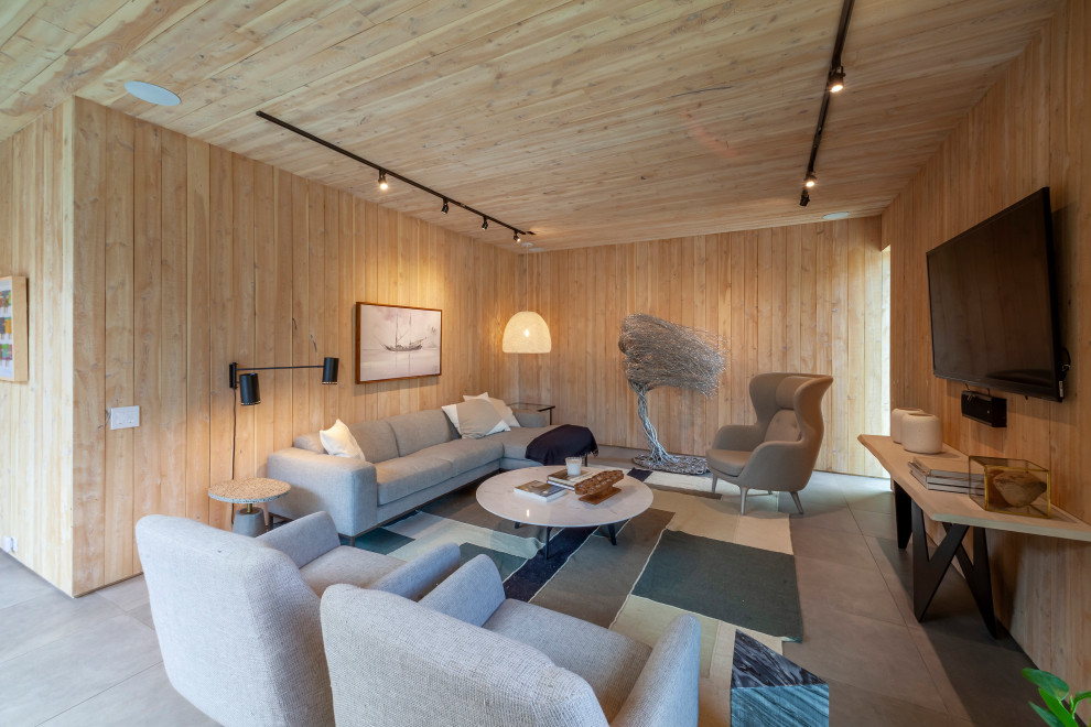На фото: большая открытая гостиная комната в современном стиле с коричневыми стенами, полом из керамической плитки, телевизором на стене, серым полом, деревянным потолком и панелями на части стены с