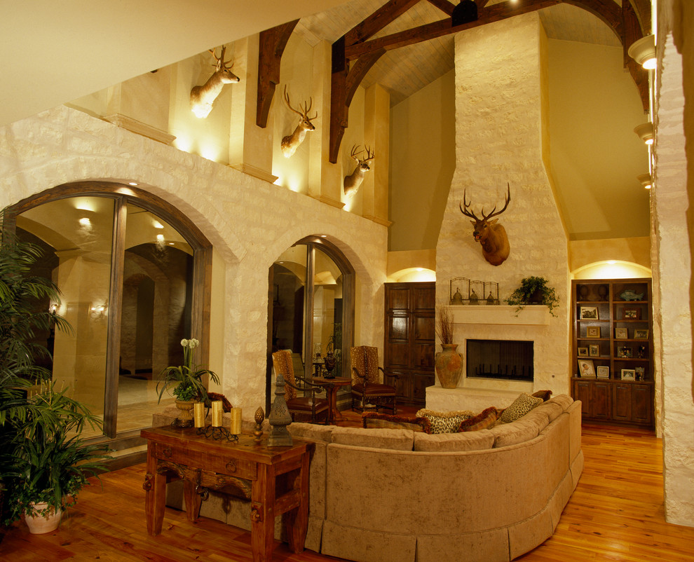 Idée de décoration pour un grand salon méditerranéen ouvert avec une salle de réception, un mur beige, un sol en bois brun, une cheminée standard, un manteau de cheminée en pierre et un sol marron.