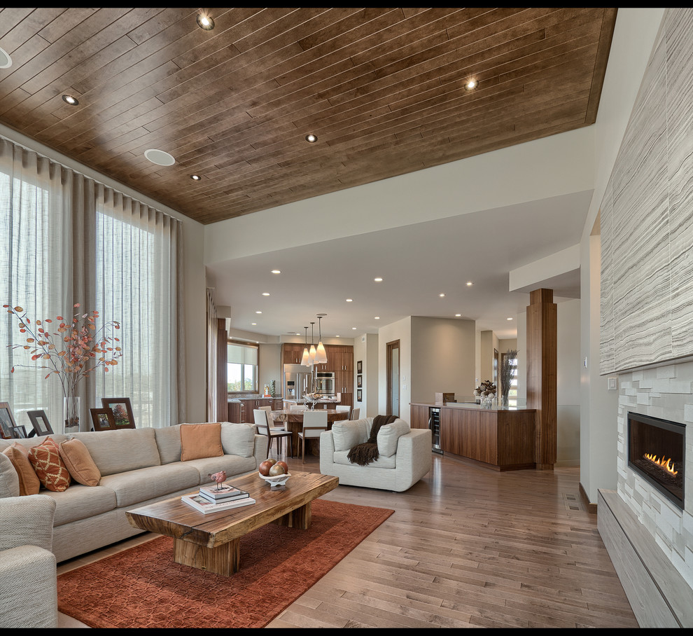 Diseño de salón abierto contemporáneo grande sin televisor con paredes beige, suelo de madera en tonos medios, chimenea lineal, marco de chimenea de piedra y suelo marrón