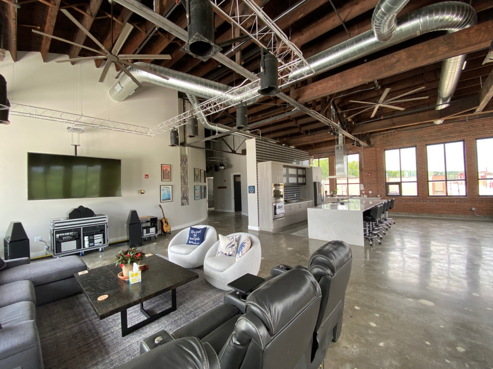 Geräumiges Industrial Wohnzimmer im Loft-Stil mit grauer Wandfarbe, Betonboden, TV-Wand, grauem Boden, freigelegten Dachbalken und Ziegelwänden in Kansas City