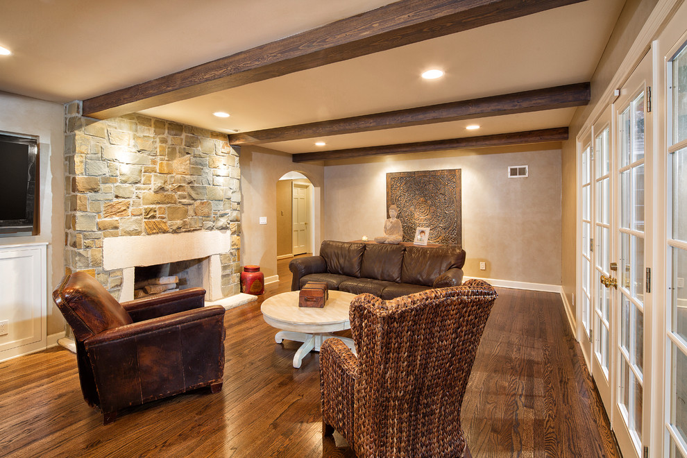 Cette image montre un salon chalet avec une cheminée standard, un manteau de cheminée en pierre, un sol en bois brun et un mur beige.
