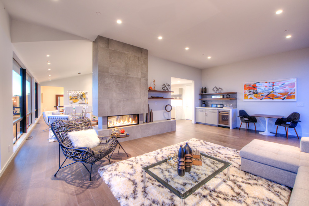 Example of a large beach style open concept light wood floor and brown floor living room design in San Francisco with a bar, gray walls, a tile fireplace and a standard fireplace