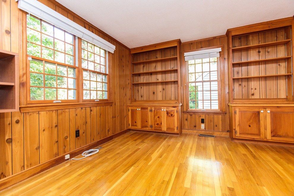 Cette image montre un grand salon traditionnel fermé avec une bibliothèque ou un coin lecture, un sol en bois brun, une cheminée standard et un manteau de cheminée en brique.