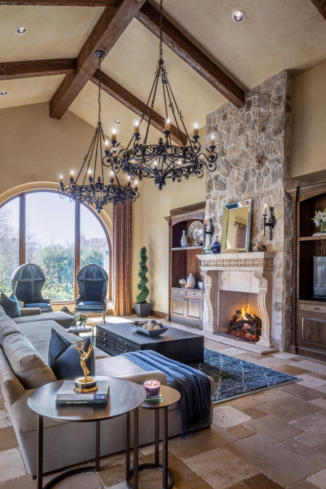 Expansive traditional open plan living room in Houston with beige walls, travertine flooring, a standard fireplace, a stone fireplace surround, a freestanding tv, beige floors and exposed beams.