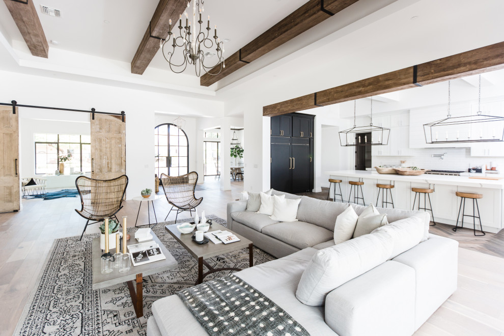 Modelo de salón abierto clásico renovado con paredes blancas, suelo de madera clara, suelo beige y vigas vistas