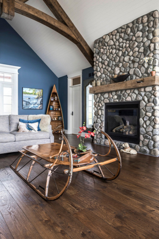 Idées déco pour un grand salon montagne ouvert avec un mur bleu, un sol en bois brun, une cheminée standard, un manteau de cheminée en pierre et un sol marron.