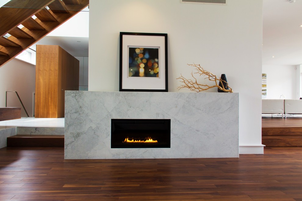 Modelo de salón abierto moderno con paredes blancas, suelo de madera en tonos medios, marco de chimenea de piedra, chimenea lineal y suelo marrón