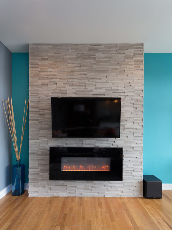 Diseño de salón abierto actual grande con paredes azules, suelo de madera en tonos medios, chimenea lineal, marco de chimenea de piedra y televisor colgado en la pared