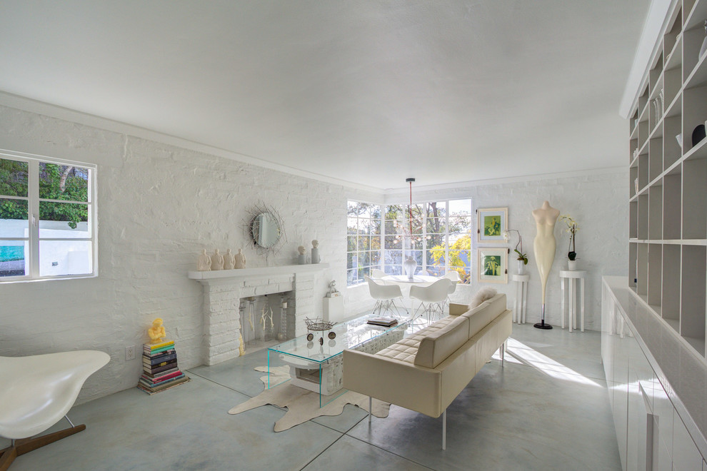 Inredning av ett modernt vardagsrum, med vita väggar, betonggolv, en standard öppen spis och en spiselkrans i tegelsten