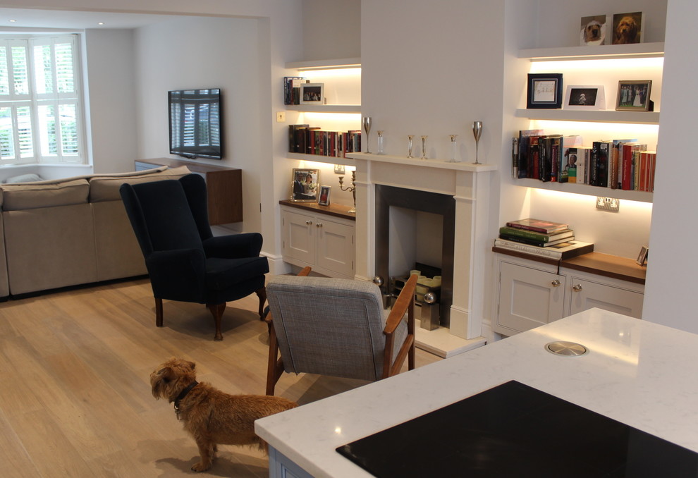 Exemple d'un salon chic de taille moyenne et ouvert avec une bibliothèque ou un coin lecture, un mur gris, parquet clair, une cheminée standard, un manteau de cheminée en plâtre et un téléviseur fixé au mur.