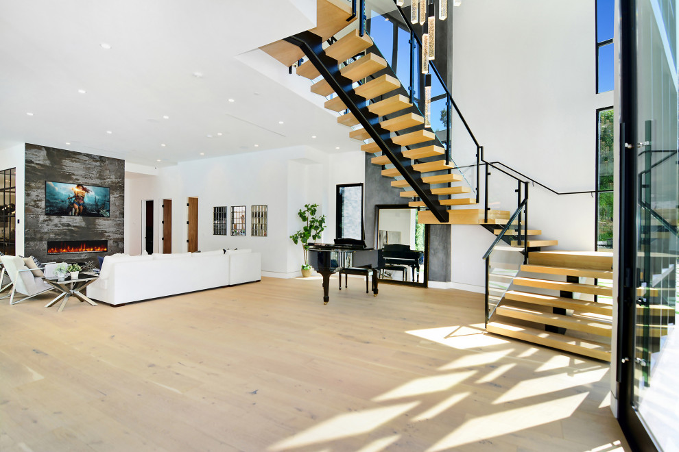 Geräumiges, Offenes Modernes Wohnzimmer mit weißer Wandfarbe, hellem Holzboden, Tunnelkamin und Kaminumrandung aus Stein in Los Angeles