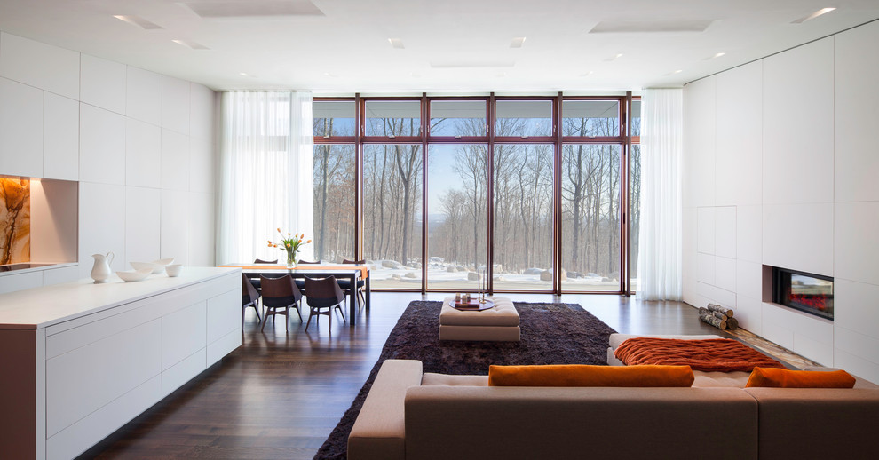 На фото: открытая гостиная комната в стиле модернизм с белыми стенами, темным паркетным полом, горизонтальным камином и красивыми шторами с
