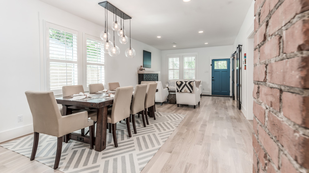 Photo of a medium sized country dining room in Houston with white walls, light hardwood flooring, a standard fireplace, a brick fireplace surround and white floors.