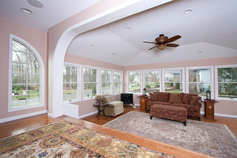 Cette image montre un grand salon traditionnel ouvert avec une salle de réception, un mur rose, un sol en bois brun et aucune cheminée.