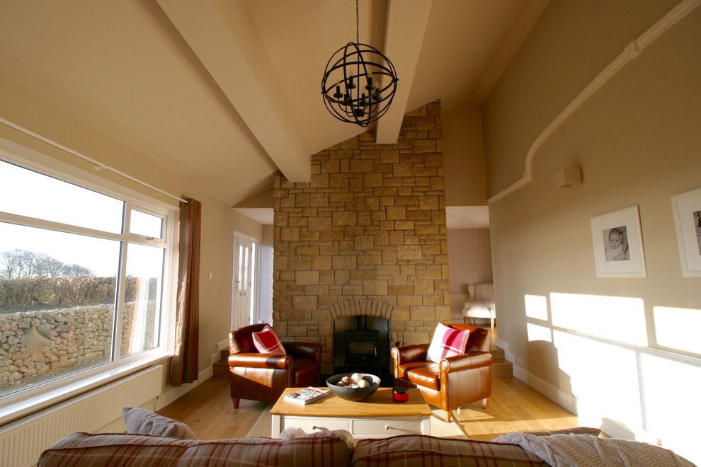 Modelo de salón abierto de estilo de casa de campo grande sin televisor con paredes marrones, suelo laminado, estufa de leña y marco de chimenea de piedra