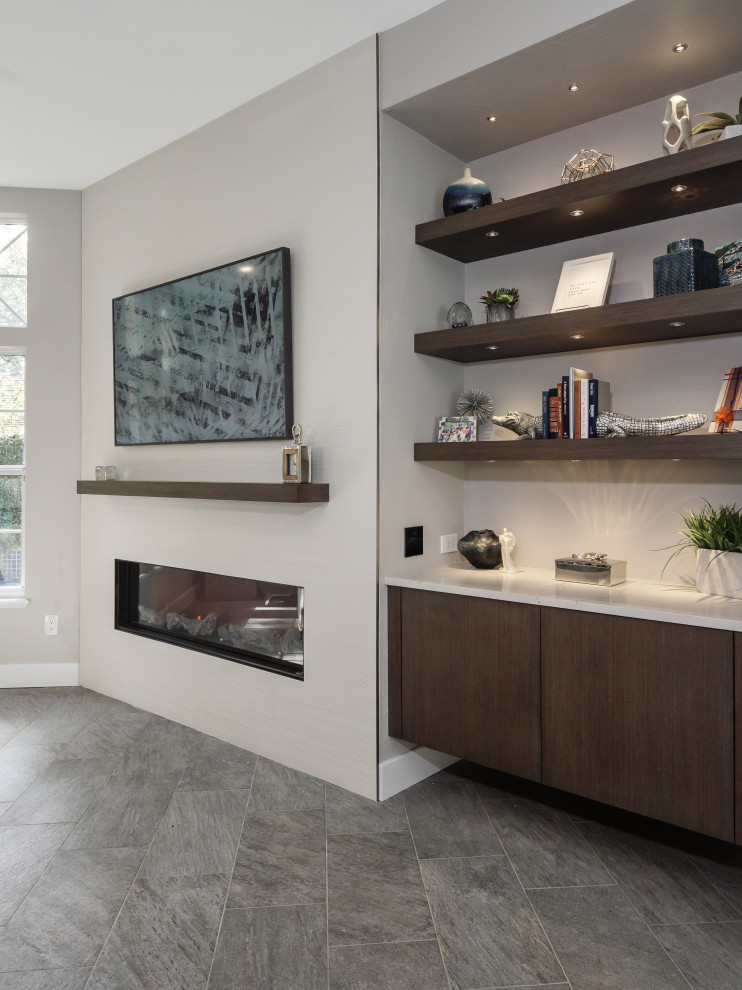 Идея дизайна: открытая гостиная комната среднего размера в стиле модернизм с с книжными шкафами и полками, серыми стенами, полом из керамогранита, подвесным камином, фасадом камина из плитки и серым полом