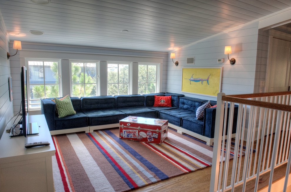 Cette photo montre un grand salon mansardé ou avec mezzanine bord de mer avec un mur bleu, un sol en bois brun et un téléviseur indépendant.